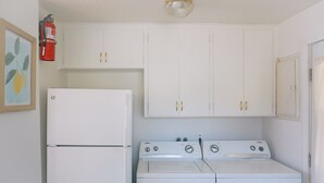 Cuina compacta amb electrodomèstics blancs, incloent-hi un frigorífic, fogó i rentadora, i armaris blancs amb nombrosos tiradors daurats.