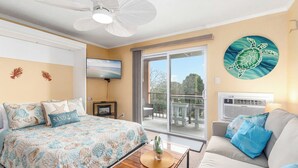 A bedroom with a bed, a ceiling fan, a TV, a balcony with a view, and a wall painting of a turtle.