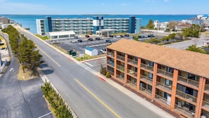 A hotel with a parking lot, a road with a pedestrian crossing, and a view of the sea.