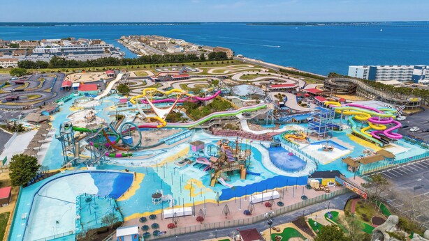 An aerial view of a water park with various slides and pools, surrounded by buildings and a body of water.