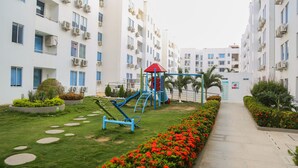 Un patio con un parque infantil, un sendero y un edificio con varios balcones y unidades de aire acondicionado.