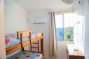 A bunk bed with floral bedding, a window with curtains, and an air conditioning unit. - Atardecer by Olamar Living (Coveñas)