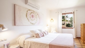 A bedroom with a bed, a bedside table, a lamp, a painting, and a window with curtains. - Villa MAESO, sea views, air conditioning, pool, 8 pax (Son Bou)