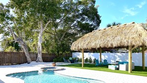 A backyard with a swimming pool, a thatched-roof gazebo, and green outdoor furniture. - Blue Bayou - Charming home with heated pool, tiki and OPTIONAL BOAT DOCKAGE (Bradenton)
