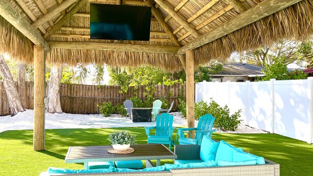 A covered patio with a thatched roof, outdoor furniture, and a flat-screen TV. - Blue Bayou - Charming home with heated pool, tiki and OPTIONAL BOAT DOCKAGE (Bradenton)