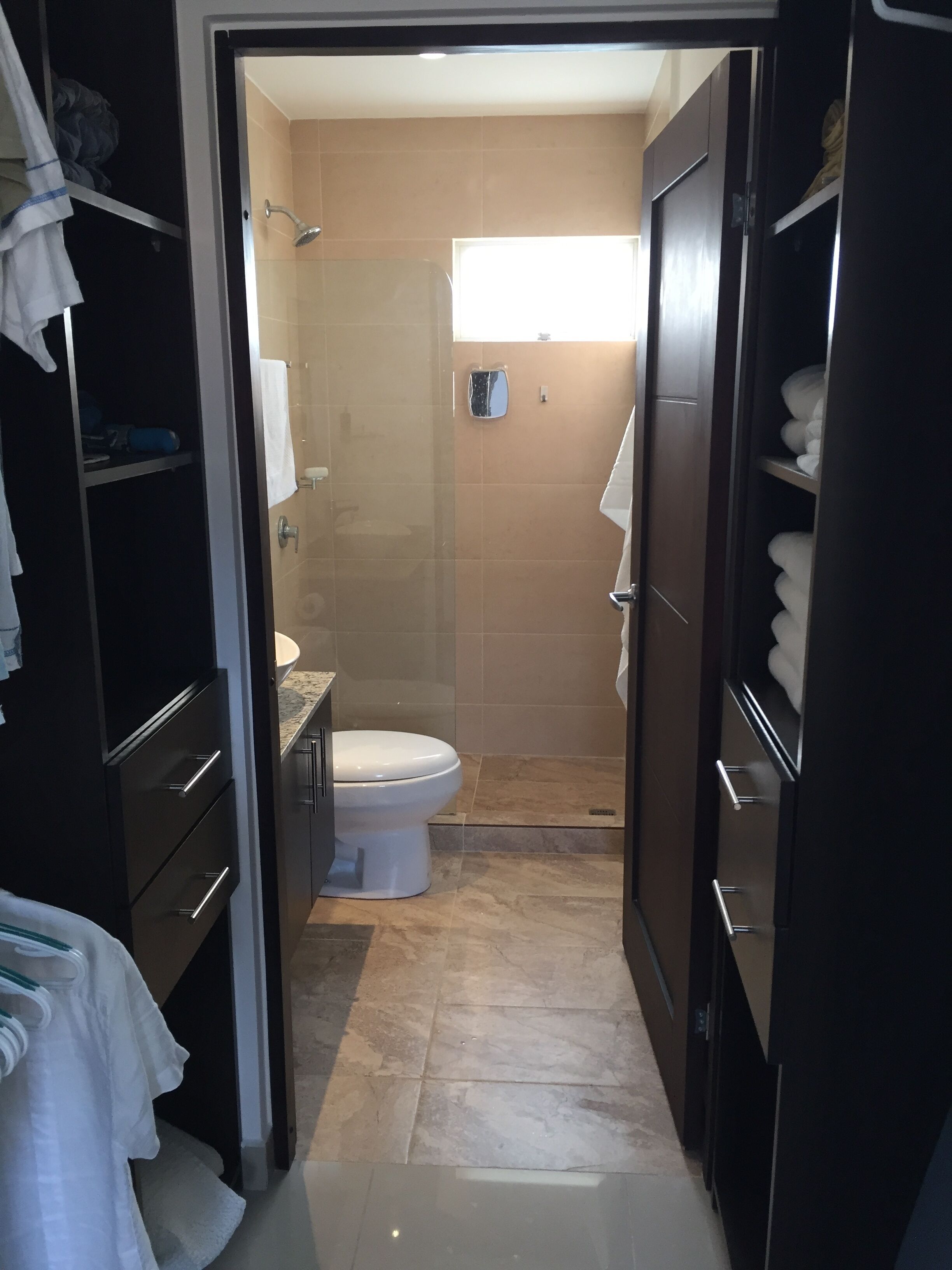 A bathroom with a toilet, a shower, and a sink. There are towels and a mirror on the wall.