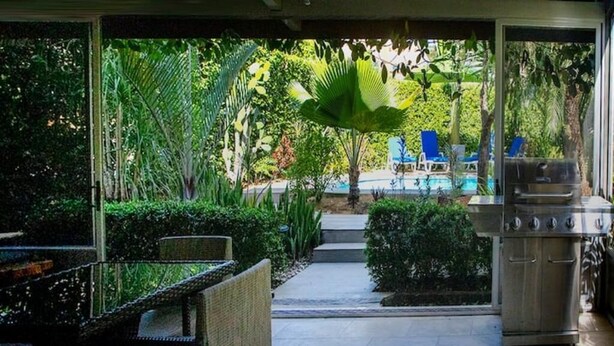 Un espace extérieur aménagé en terrasse, avec un barbecue, une table à manger et des chaises, donnant accès à une zone piscine avec des chaises longues.