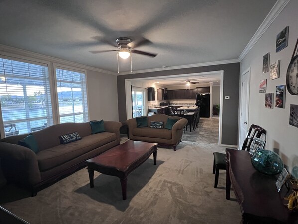 A living room with a brown sofa, a coffee table, and a view of a kitchen and dining area through an open door. - The One More
On the water with semi private beach and launch (Mohave Valley)