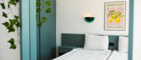 Quarto de hotel com cama, mesa de cabeceira, guarda-roupa verde e uma luminária fixa na parede.