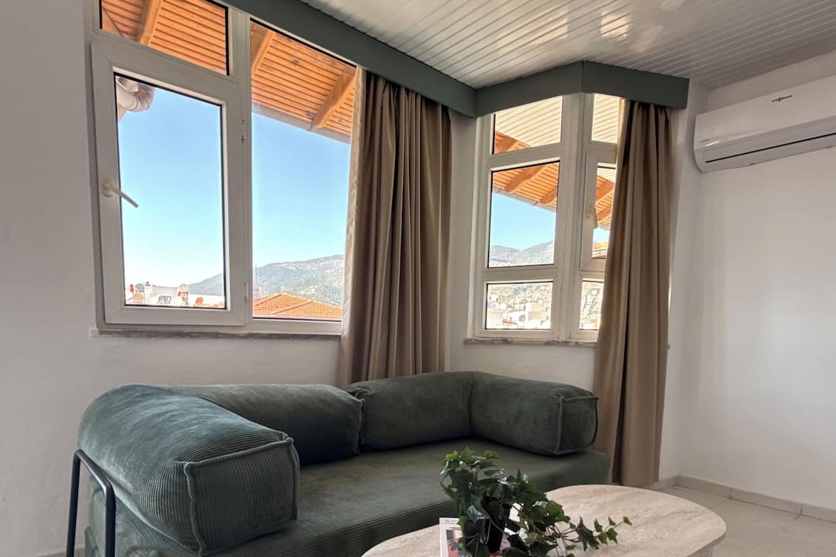 Una sala de estar moderna con un sofá verde, una mesa de centro de mármol y ventanas grandes con cortinas.