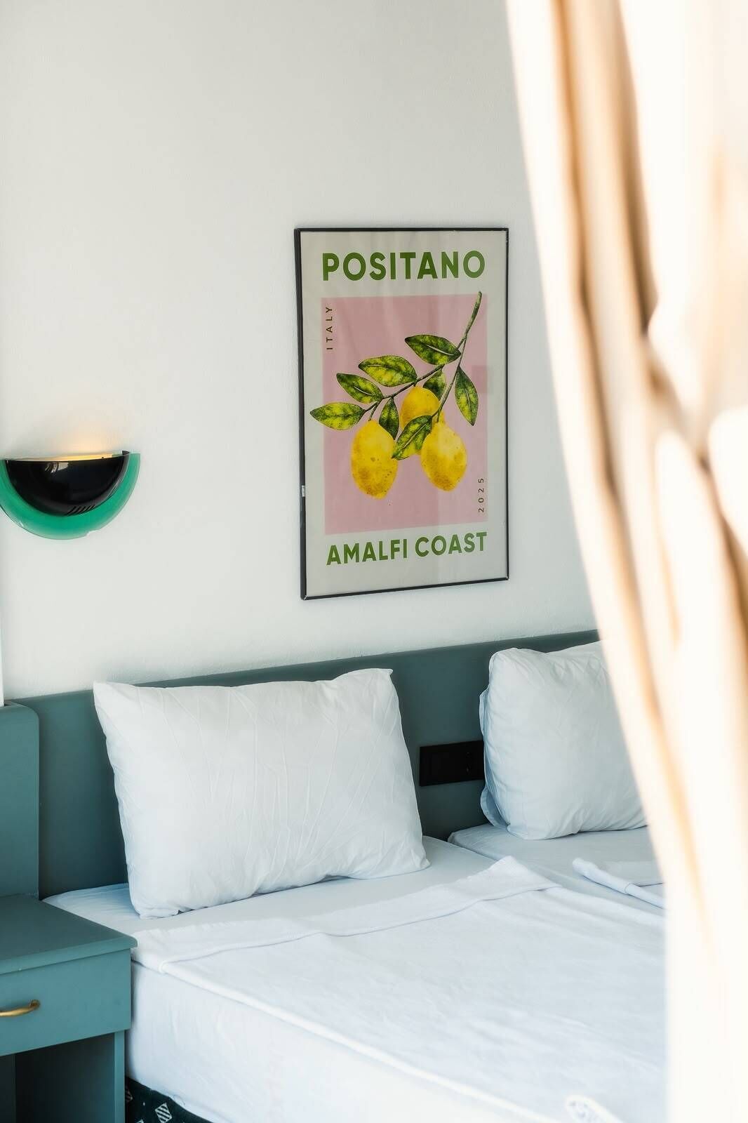A hotel room with a bed, two pillows, a nightstand, a wall-mounted light, and a framed picture of lemons.