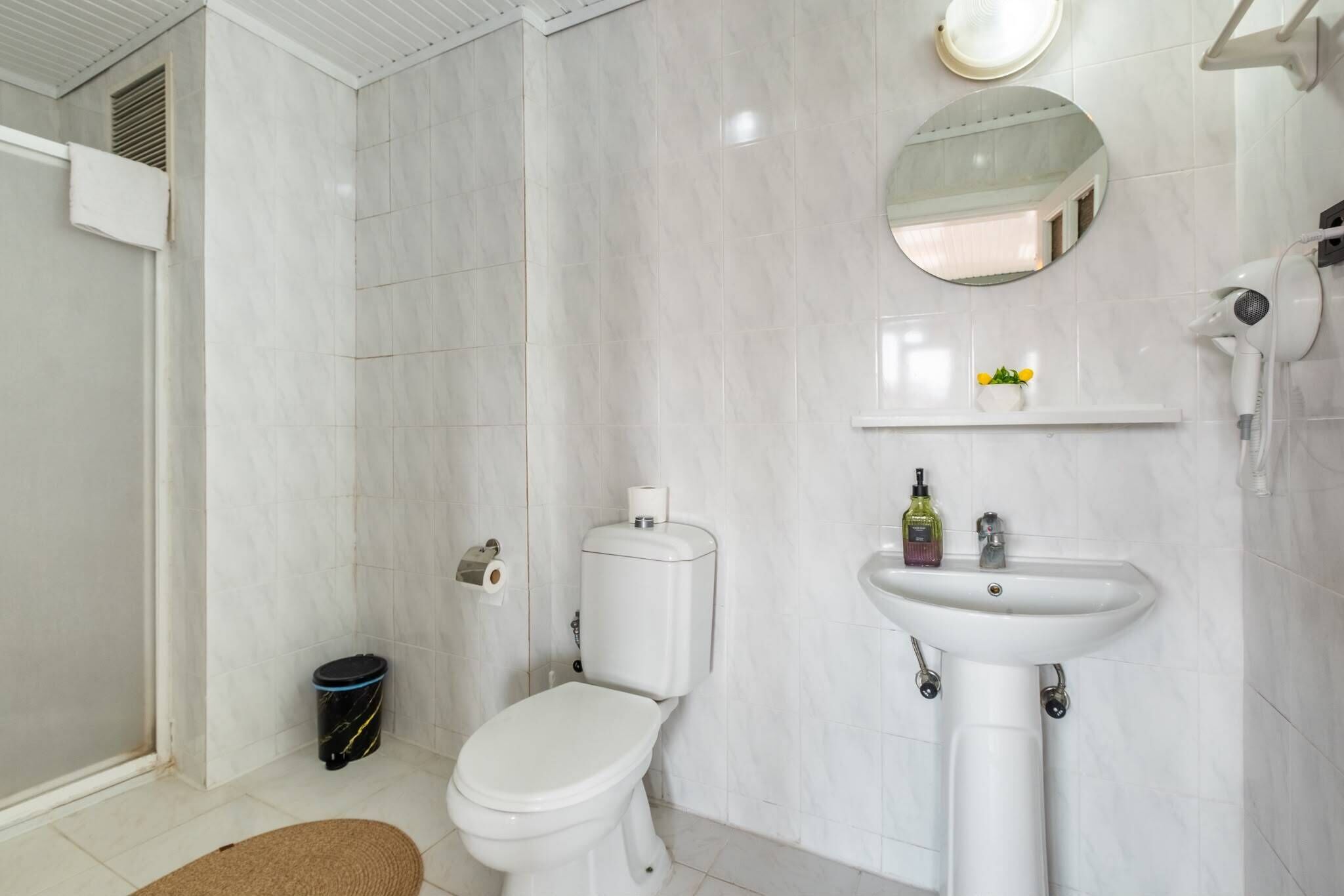 A bathroom with a toilet, sink, mirror, and a small trash bin.
