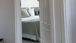A narrow hallway leading to a bed with a headboard and pillows, a wall-mounted light fixture, and a door with a white frame. - Casa Cleo Suite (Alanya)