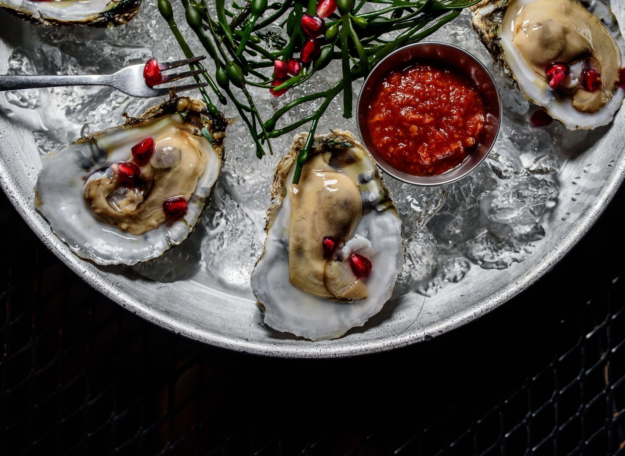 Een bord oesters met granaatappelpitten en een schaaltje saus.
