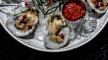 Een bord oesters met granaatappelpitten en een schaaltje saus.
