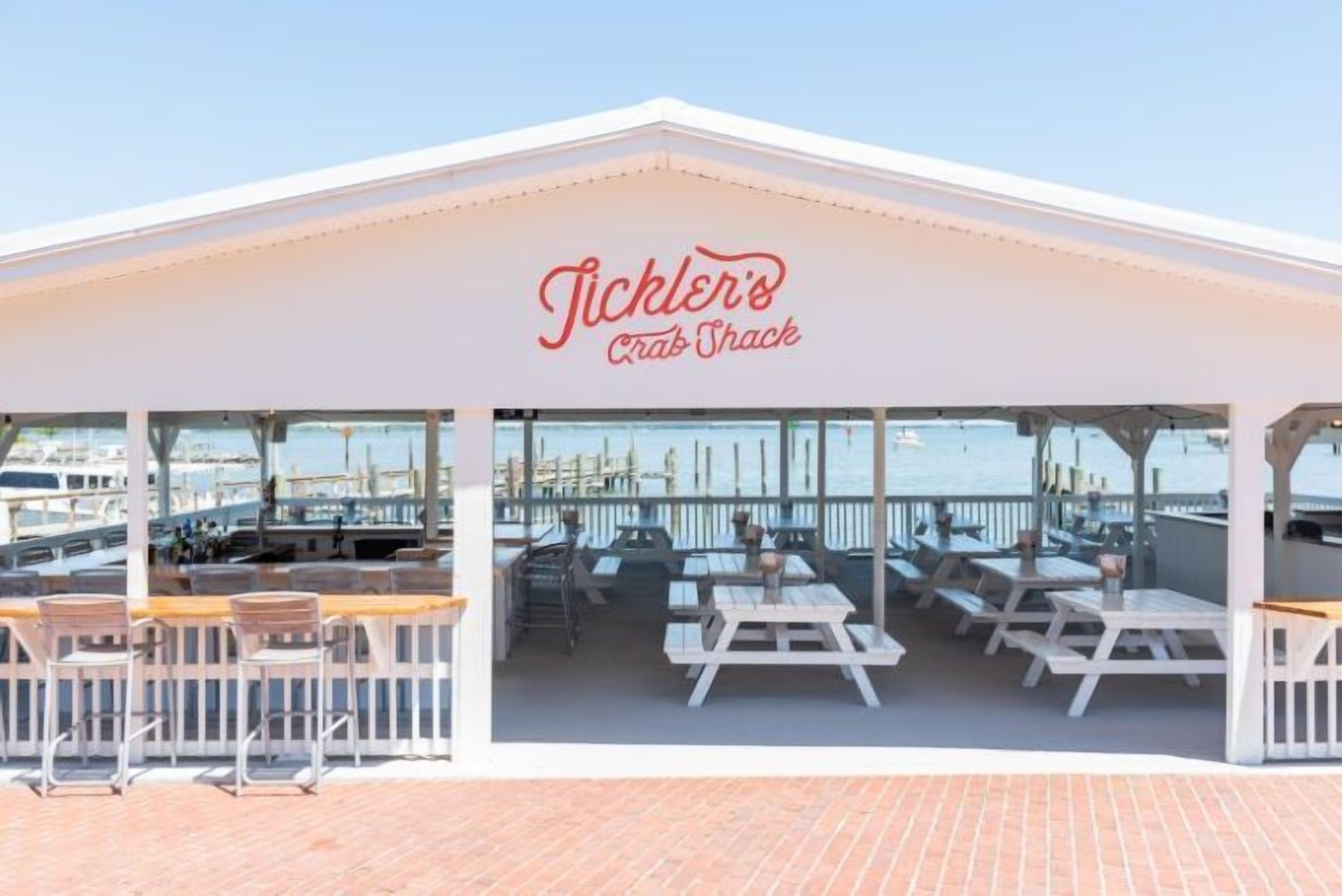 A covered outdoor seating area with tables and chairs, a railing, and a view of the marina.