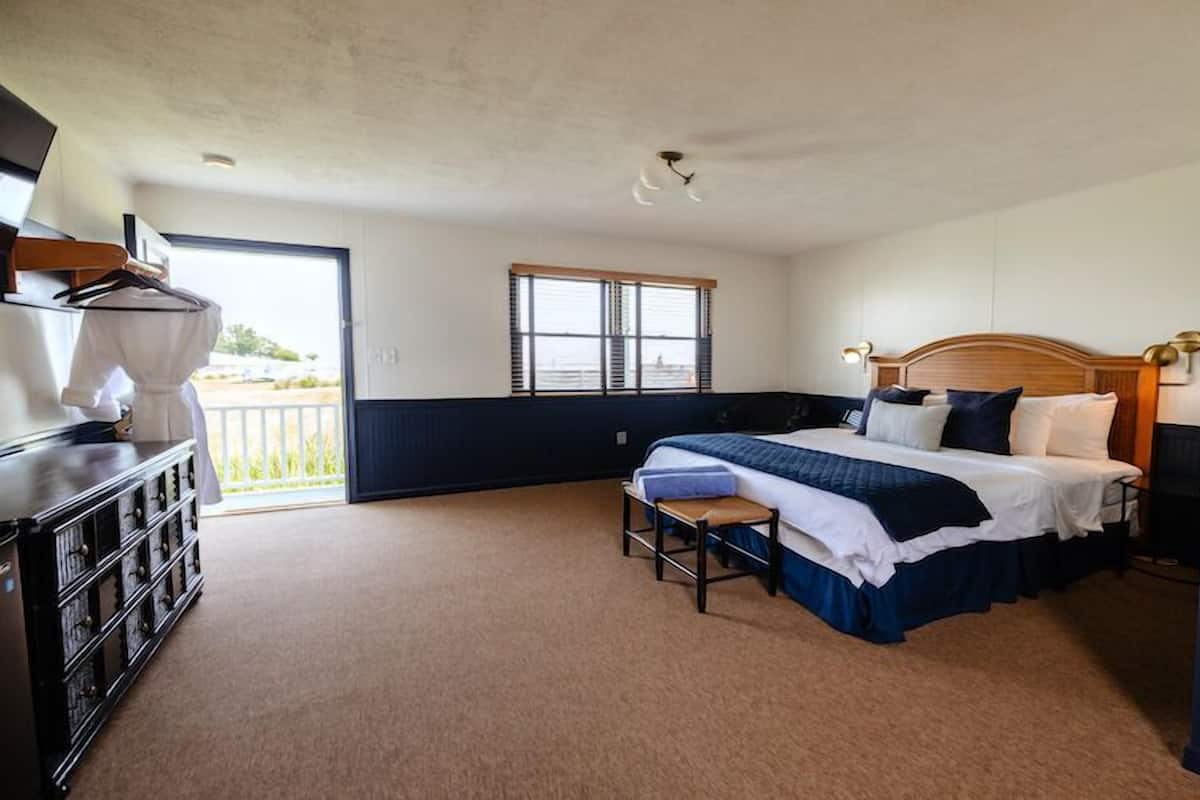 Une chambre à coucher comprenant un lit, des tables de chevet, un banc, une commode et une fenêtre.