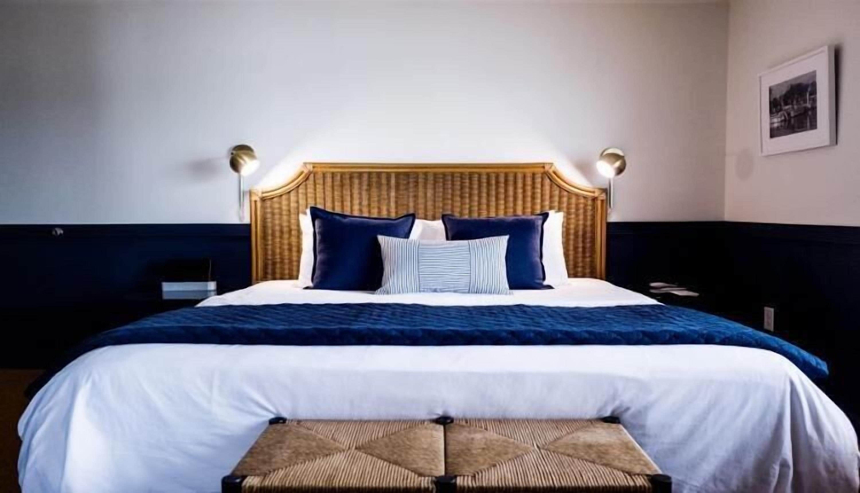 A neatly made bed with a wooden headboard, two bedside lamps, and a framed picture on the wall.