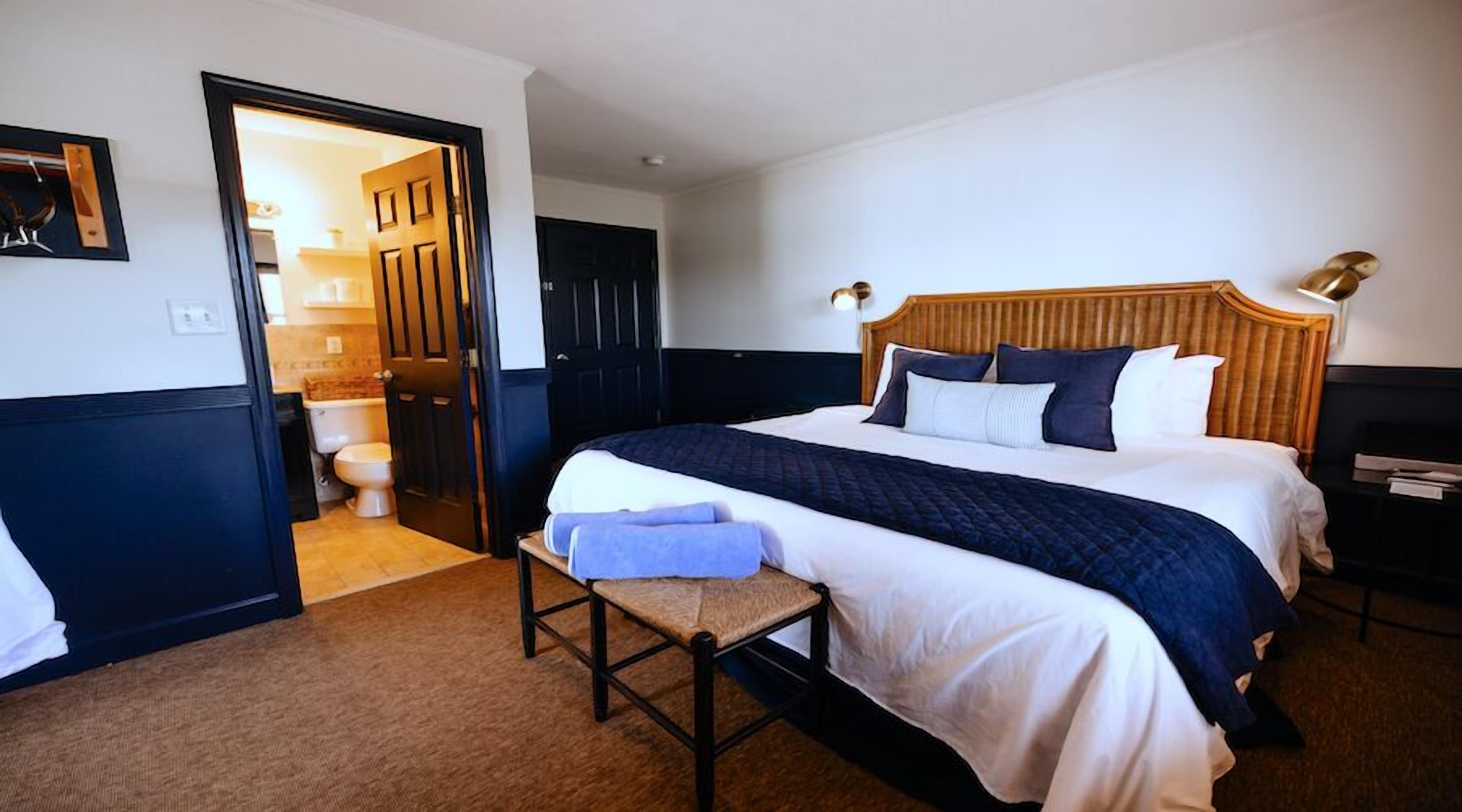 A hotel room with a large bed, a wooden headboard, a bedside table, a chair, and a bathroom visible through an open door.