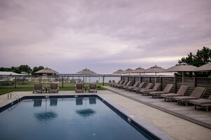A swimming pool with lounge chairs and umbrellas, surrounded by a fence and trees.