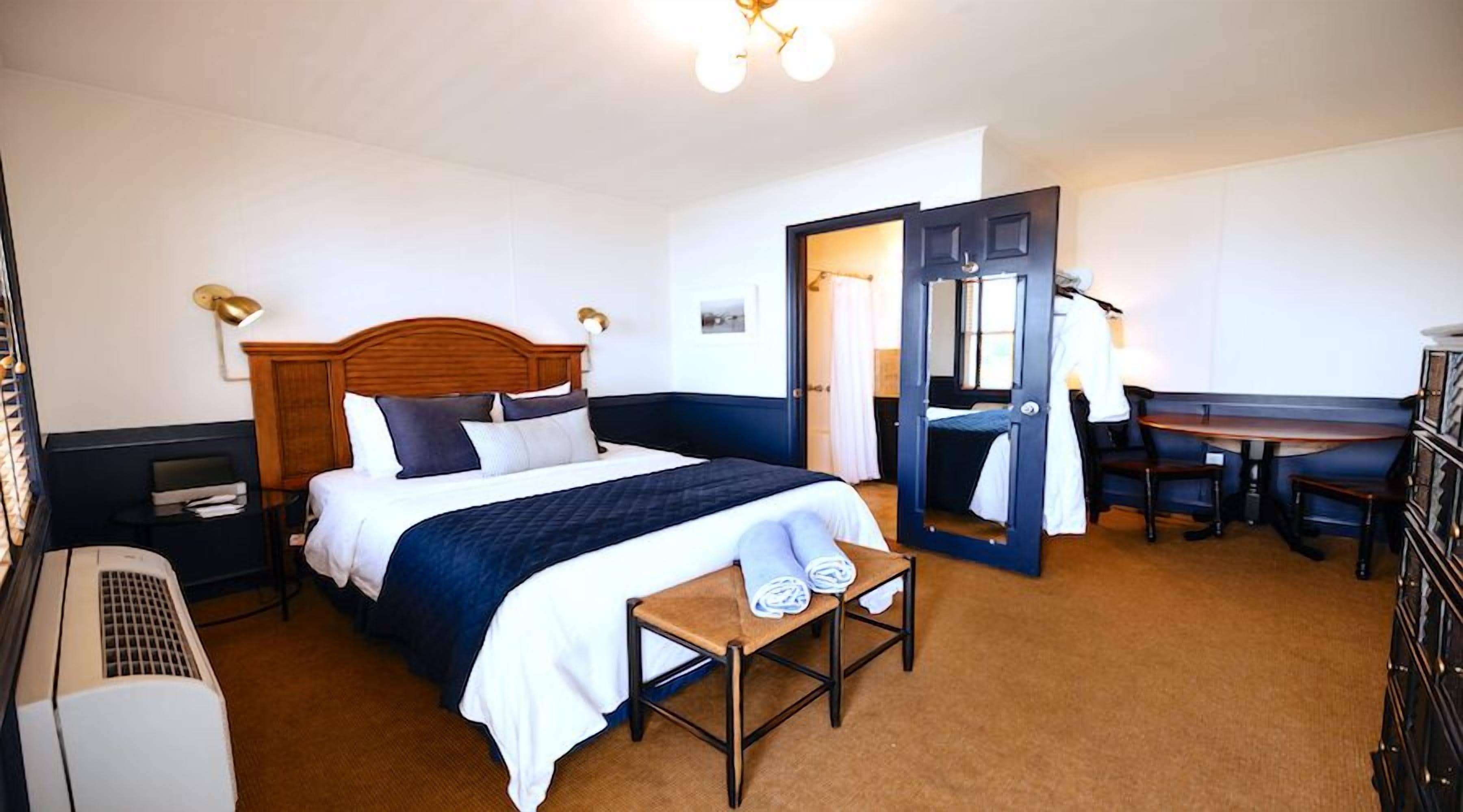 A hotel room with a bed, bedside table, desk, chair, and a wardrobe.