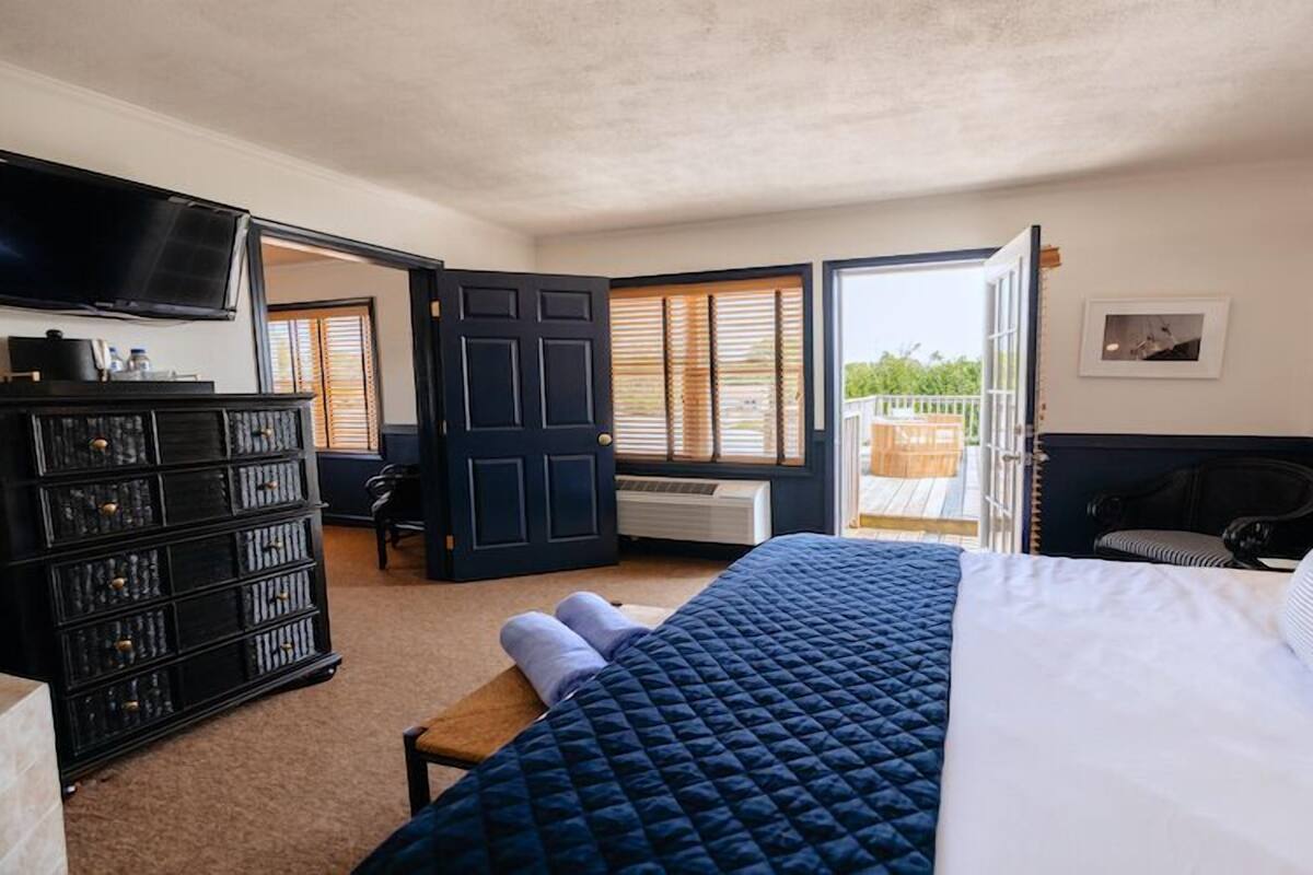 Une chambre à coucher comprenant un lit, une commode, un téléviseur et une fenêtre avec des stores.