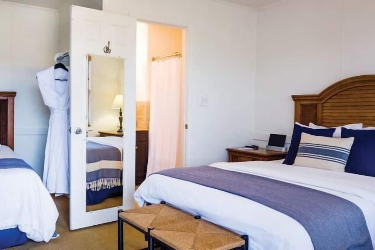 Une chambre d’hôtel avec deux lits, un banc, un bureau et un miroir.