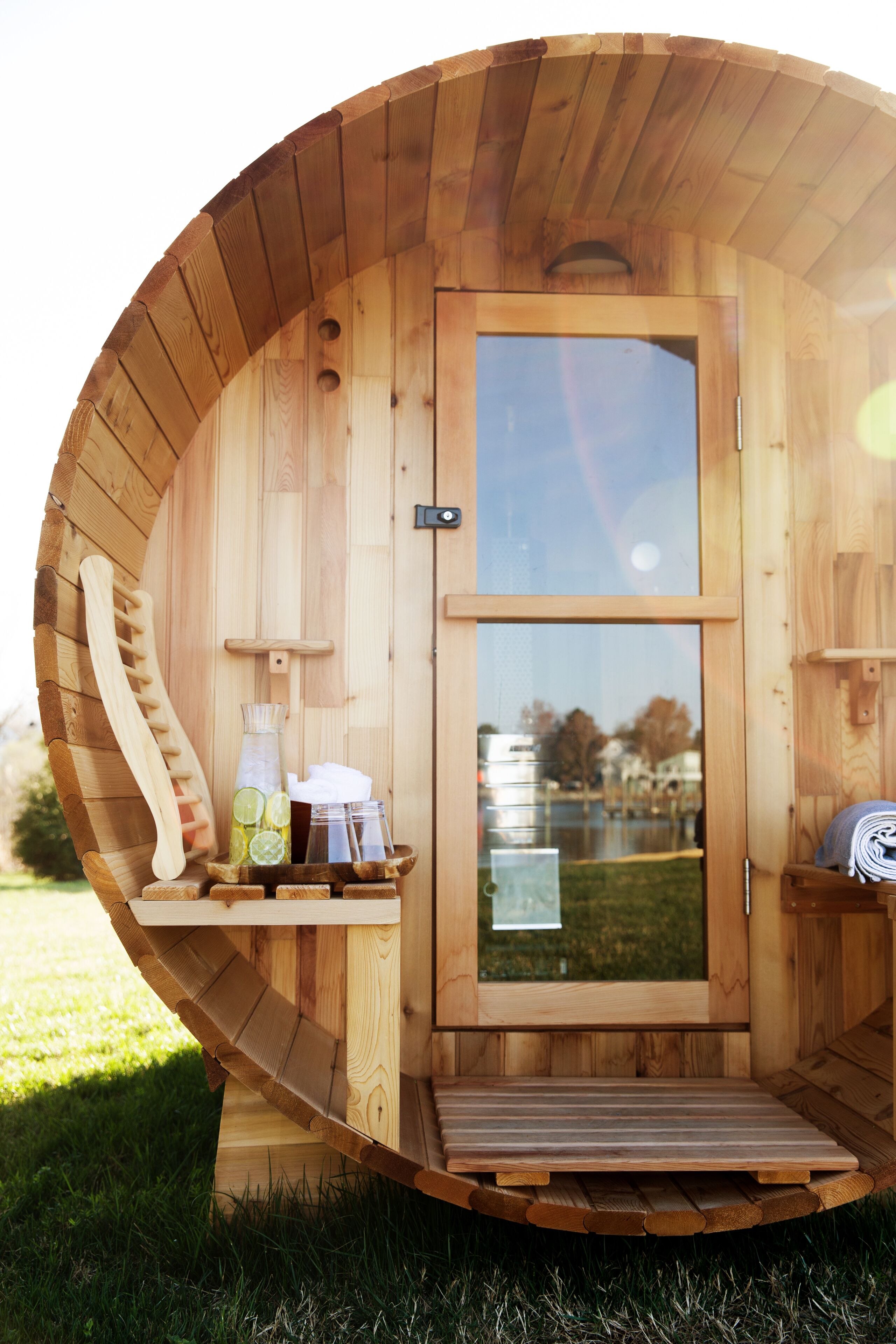 A wooden sauna with a door, a wooden bench, and a bottle of water on the bench.