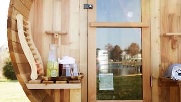 A wooden sauna with a door, a wooden bench, and a bottle of water on the bench.