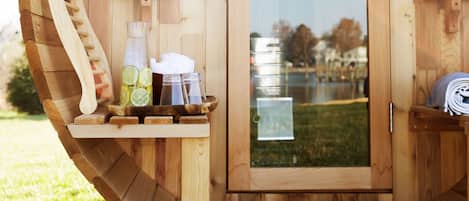 A wooden sauna with a door, a wooden bench, and a bottle of water on the bench.