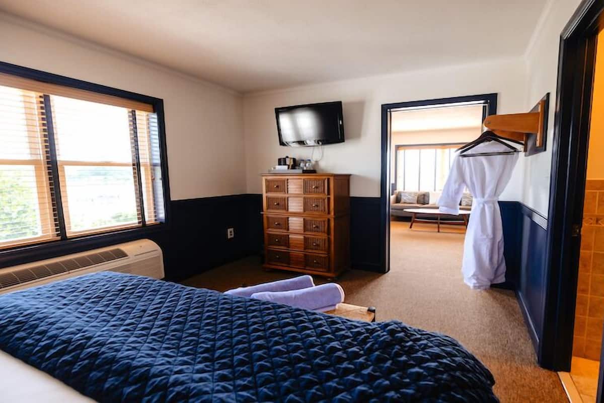 Une chambre d’hôtel avec un lit, une commode, une télévision et un peignoir accroché au mur.