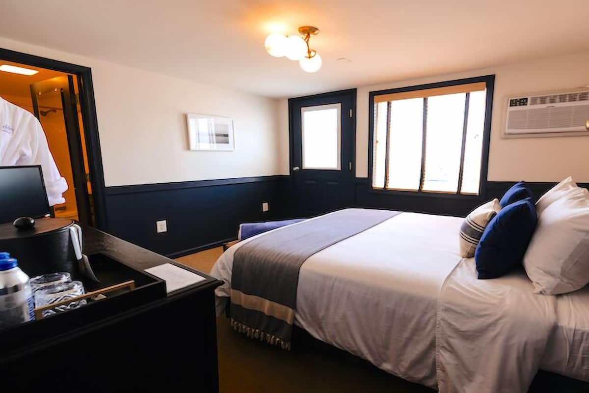Une chambre d’hôtel avec un lit, un bureau avec un ordinateur, un miroir et une fenêtre.