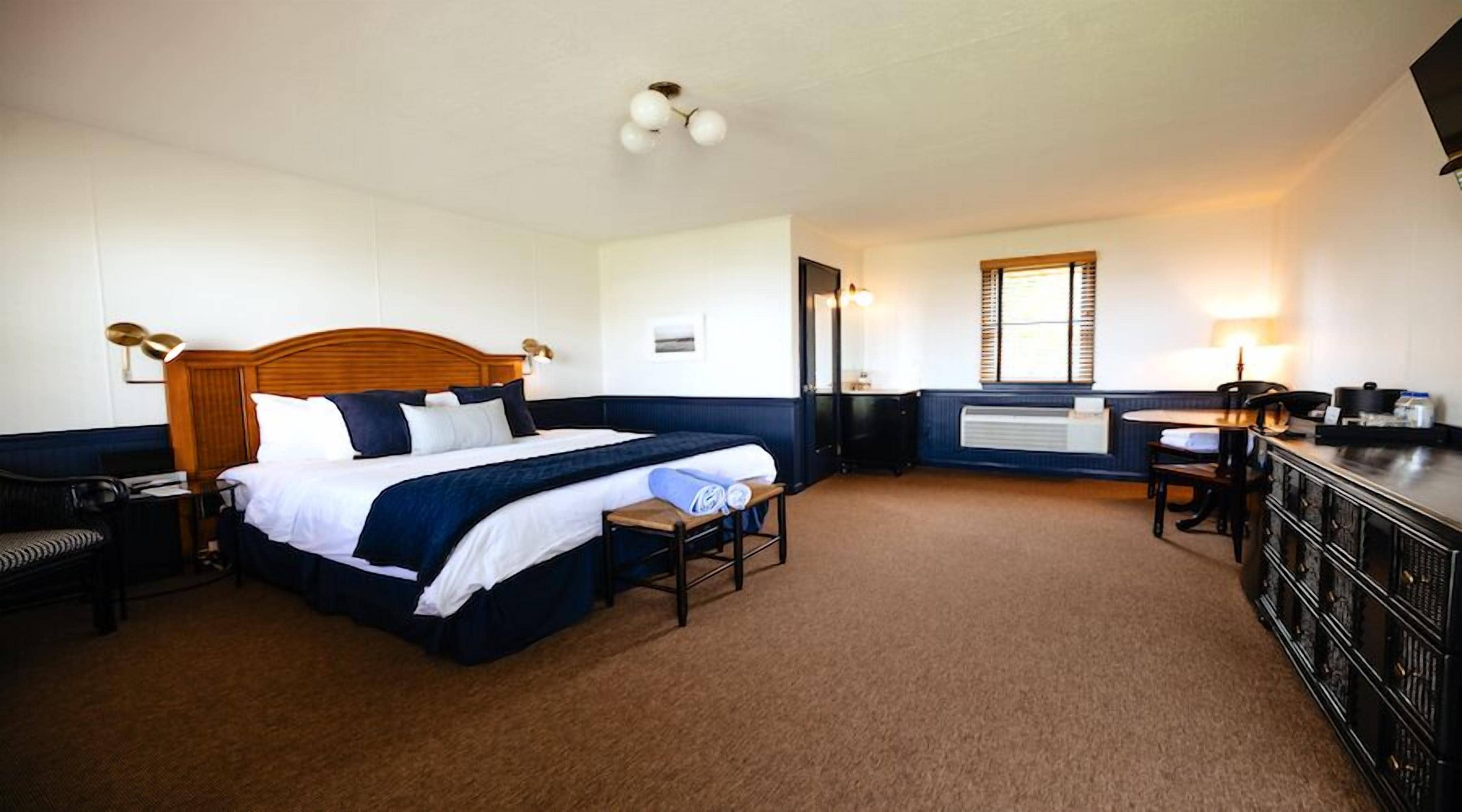 Habitación de hotel con una cama grande, un escritorio, una silla, un aparador y una ventana con persianas.