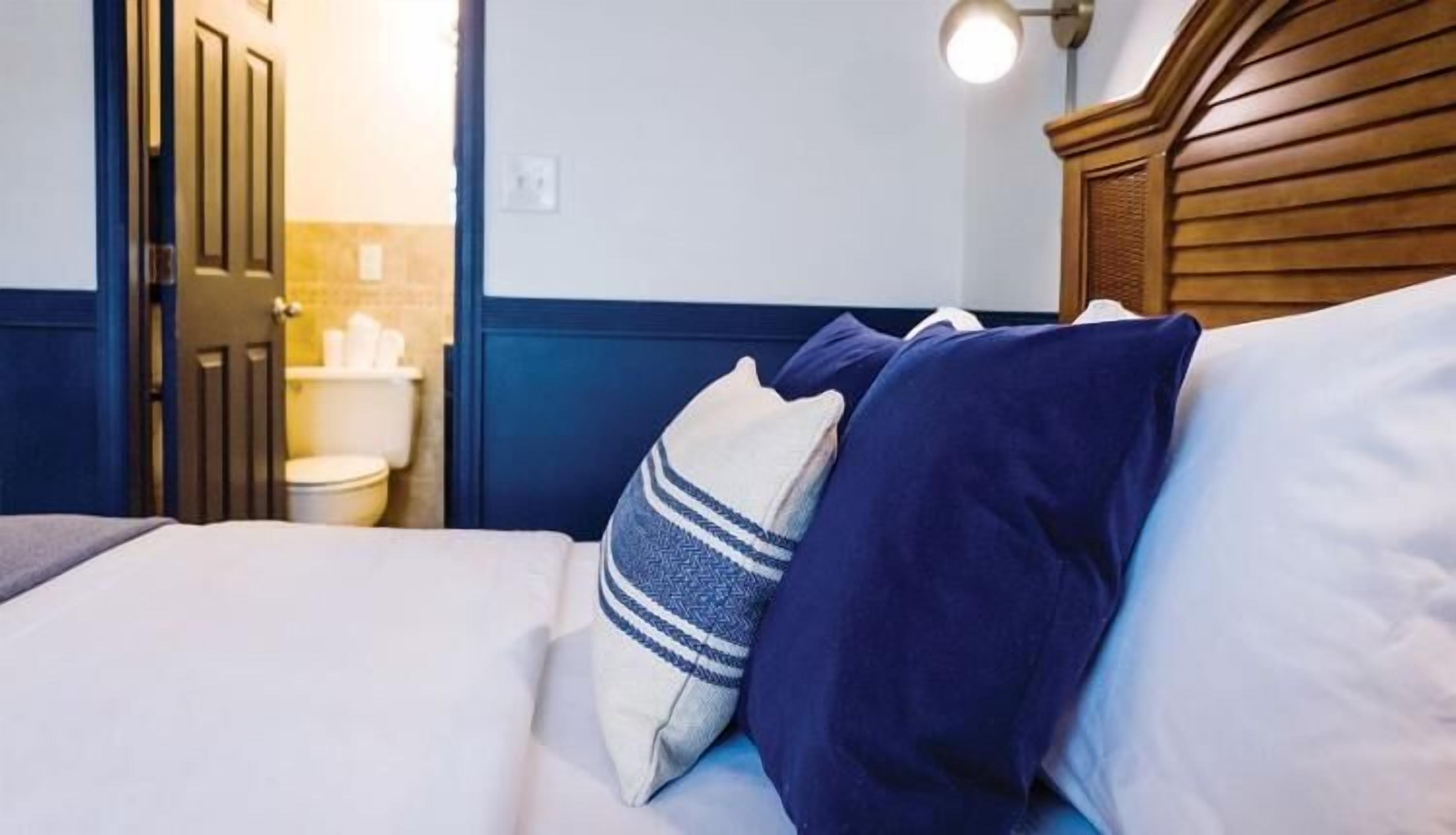 A hotel room with a bed, pillows, a wooden headboard, and a nightstand.