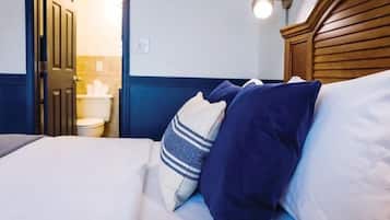 A hotel room with a bed, pillows, a wooden headboard, and a nightstand.