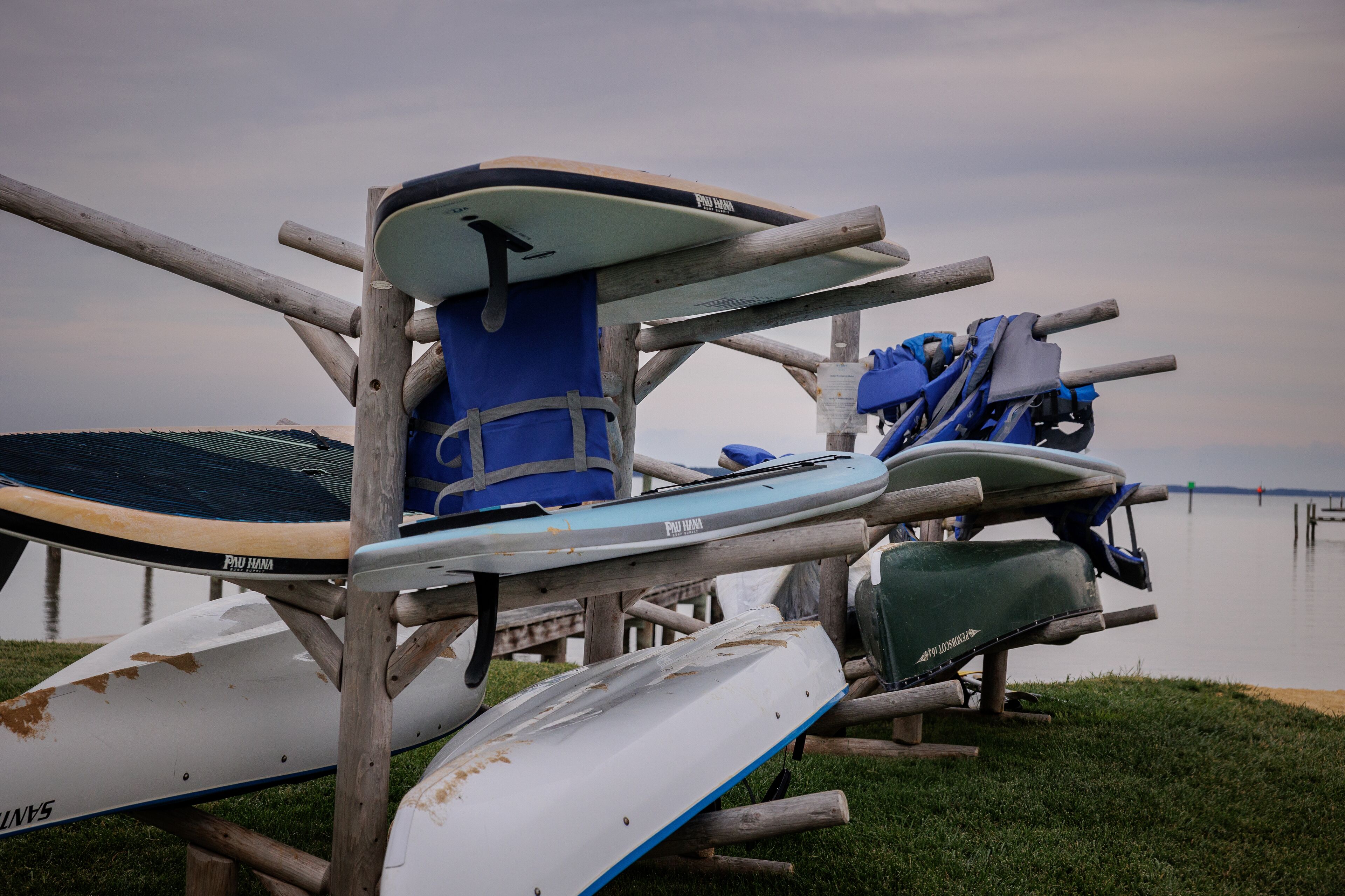 Diverse tavole da SUP impilate su un supporto di legno vicino all'acqua.