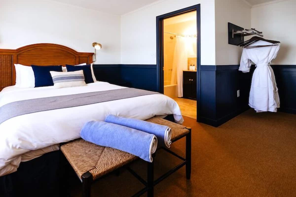 Un lit bien fait, avec une tête de lit en bois, une table de chevet avec une lampe et un peignoir suspendu à un porte-manteau.