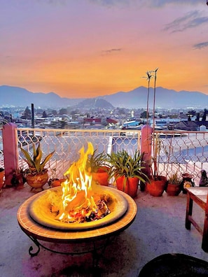 A fire pit with plants on a balcony overlooking a cityscape with mountains in the distance. - Increible Loft Terraza Y Vista (San Cristóbal de las Casas)