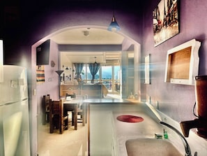 A kitchen with a central island, a dining area with chairs, and a view through an open archway.