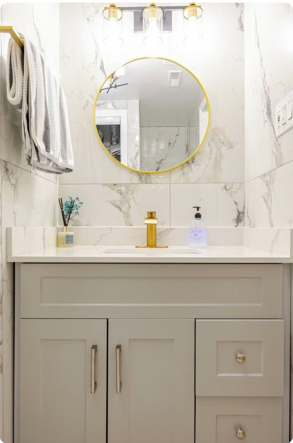 A bathroom with a marble backsplash, a gold-framed mirror, a white sink with a gold faucet, and two cabinets with gold handles.