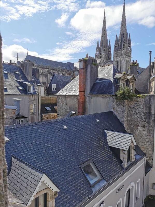 A view of a historic building with a prominent spire, surrounded by older stone buildings with slate roofs.