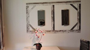 A room with a rustic wall decor, a small table with a potted orchid, and a wicker chair. - Workation-suite im Ferienpark (Altenau)