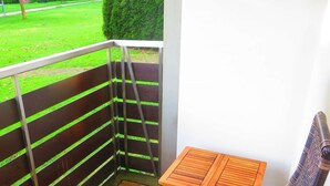A balcony with a metal railing, a small wooden table, and a view of a green lawn and hedge. - Workation-suite im Ferienpark (Altenau)