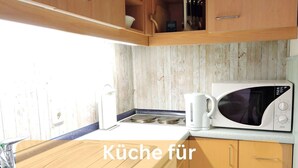 A kitchen with wooden cabinets, a microwave, and a kettle. - Workation-suite im Ferienpark (Altenau)