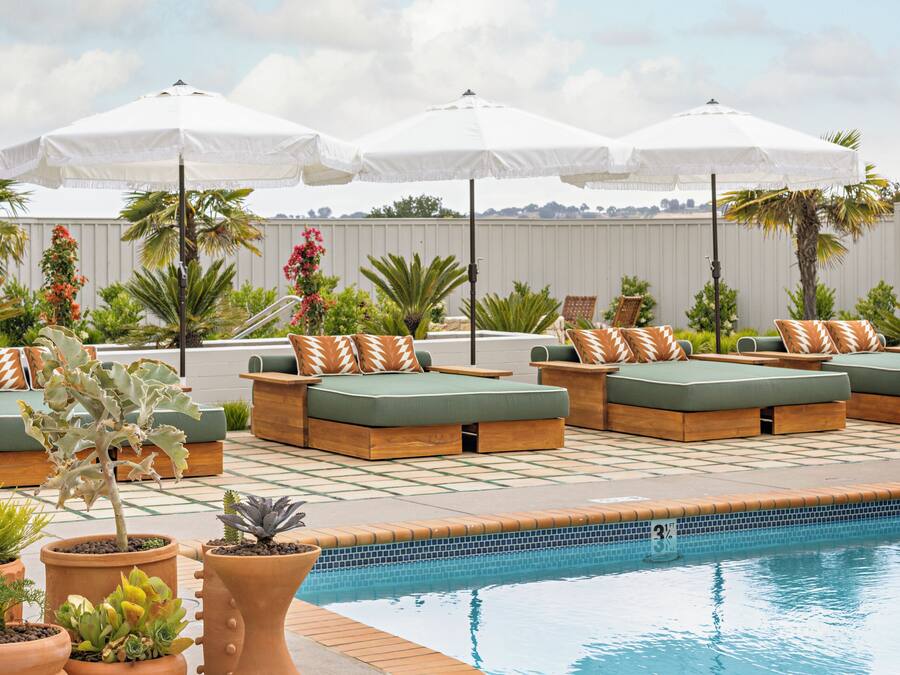 A poolside area with green cushioned seating, white umbrellas, and potted plants.