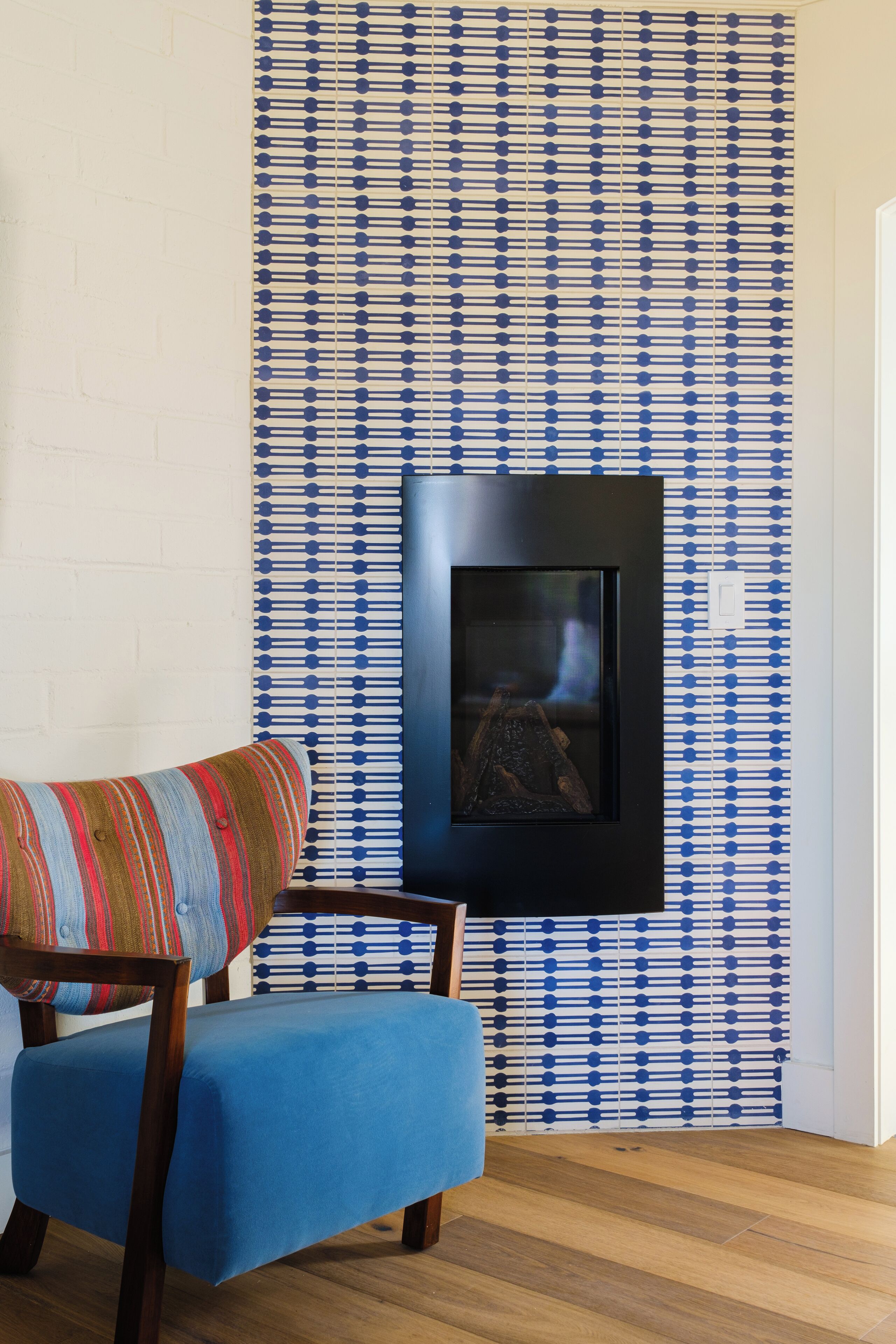 Una habitación con papel tapiz estampado, un cuadro enmarcado en la pared y un sillón tapizado en azul.