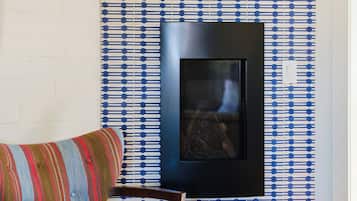 A room with a patterned wallpaper, a framed picture on the wall, and a blue upholstered chair.