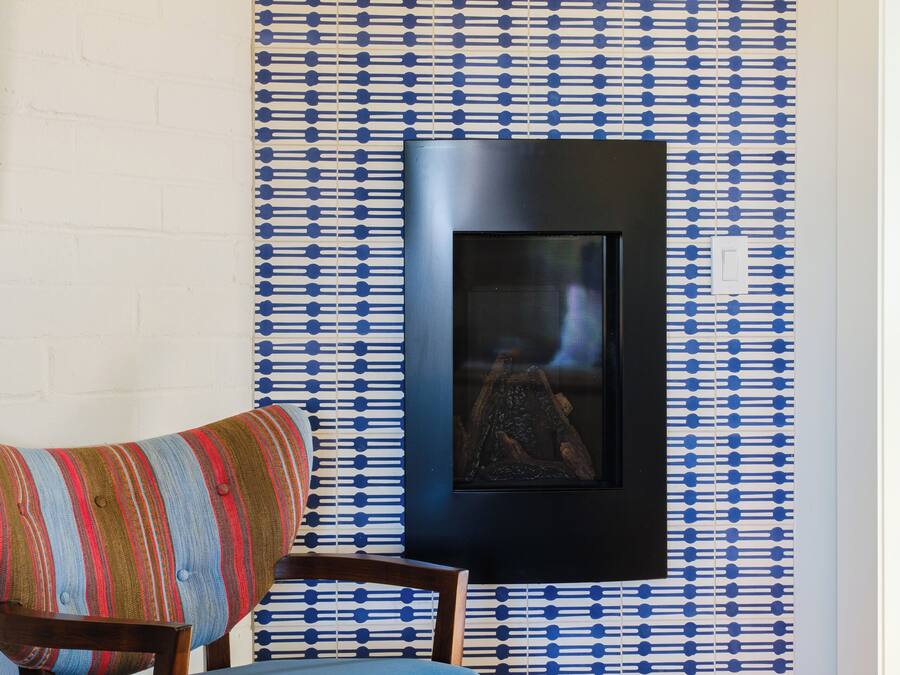 A room with a patterned wallpaper, a framed picture on the wall, and a blue upholstered chair.
