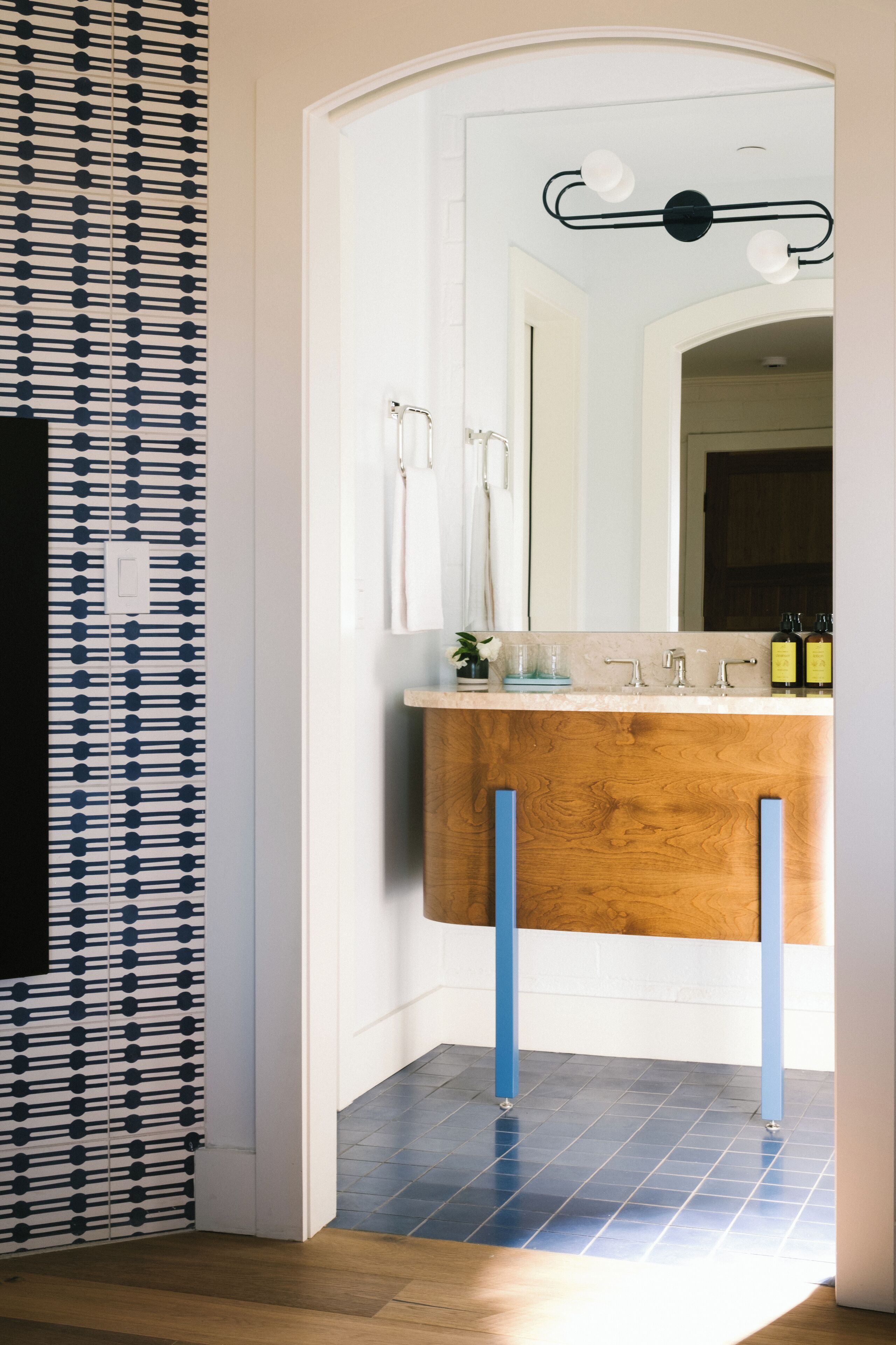 A bathroom with a wooden vanity, a mirror, and a modern light fixture.
