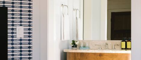 A bathroom with a wooden vanity, a mirror, and a modern light fixture.